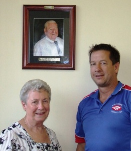 Tyntynder Football Netball Club President Mal Devereax and Shirley Looney standing in front of a photo of the club Life Member, the late Alan Looney